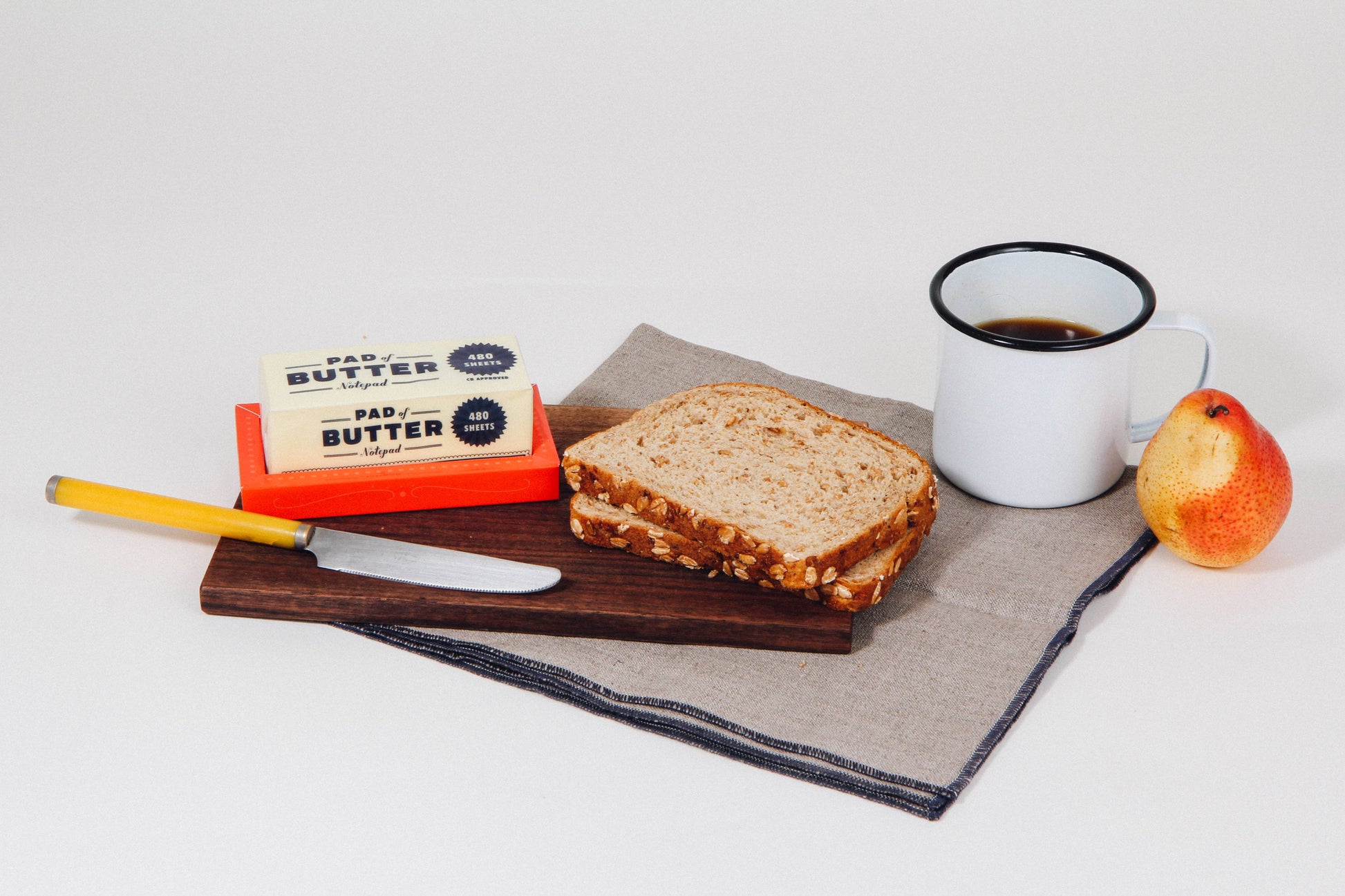Butter notepad, bread, coffee, and an apple on a white surface