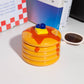 Ceramic storage jar made to look like a stack of pancakes with a decorative lid with a pad of butter and blueberries on a white background with books in background 