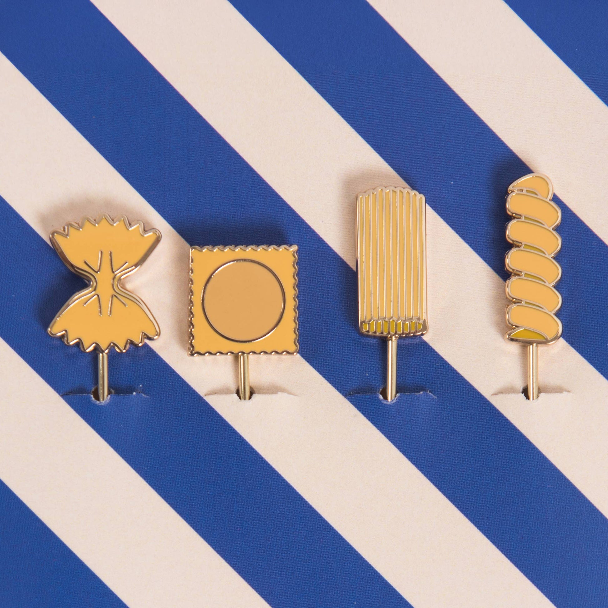 Four gold-colored pasta themed cocktail picks on a blue and white striped background
