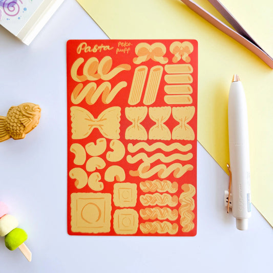 Pasta-themed sticker sheet on a red background with a pen and small toy on a light surface.