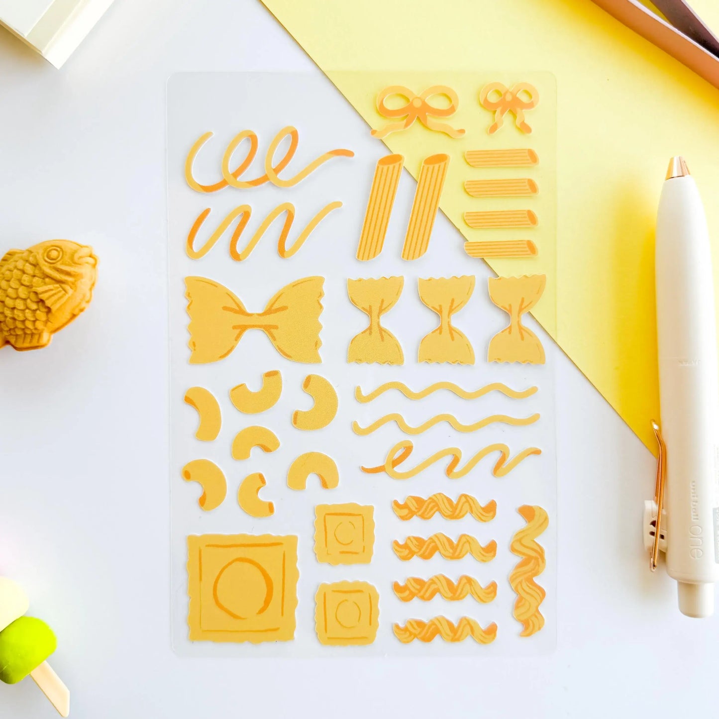 Set of yellow pasta-shaped stickers on a white surface with a pen
