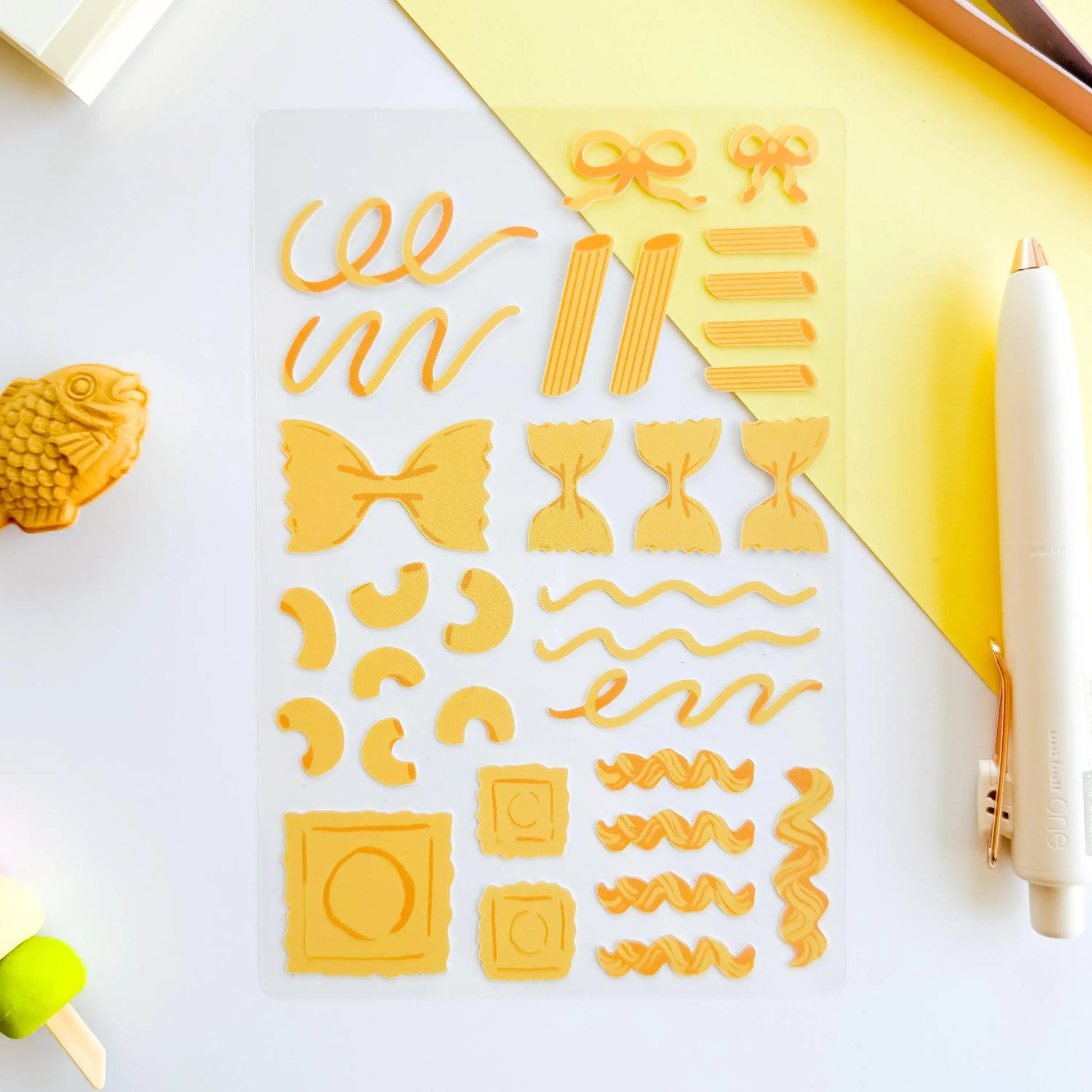 Set of yellow pasta-shaped stickers on a white surface with a pen