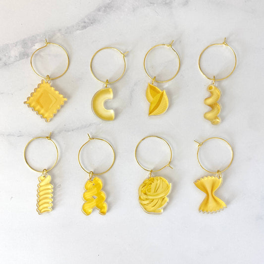 Set of 8 yellow pasta-shaped drink charms with gold ring on a marble background