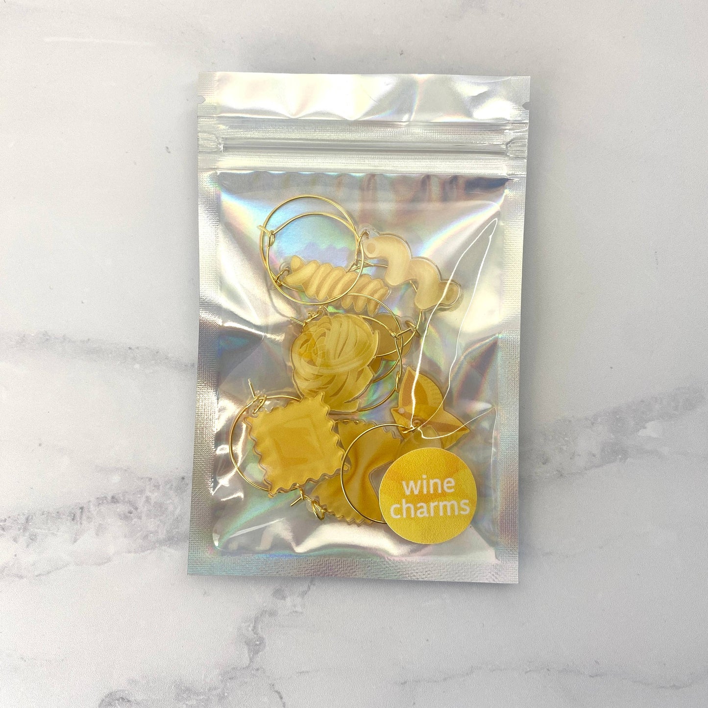 Packaged gold, pasta wine charms with a clear front bag on a marble surface