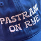 close up on blue baseball cap with white embroidered text that reads "pastrami on rye" 