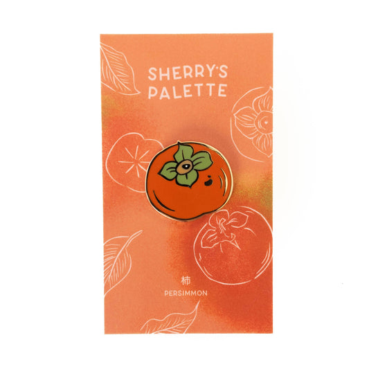 Enamel pin of a persimmon with 'Sherry's Palette' branding on an orange background.