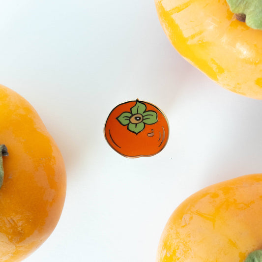 Enamel pin shaped like a persimmon fruit on a white background