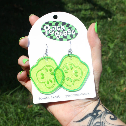 Glittery, green, acrylic, sliced pickle earrings on fish hook backings with cardboard backing/packaging