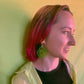 Glittery, green, acrylic, sliced pickle earrings on fish hook backings. Seen here being worn on a person
