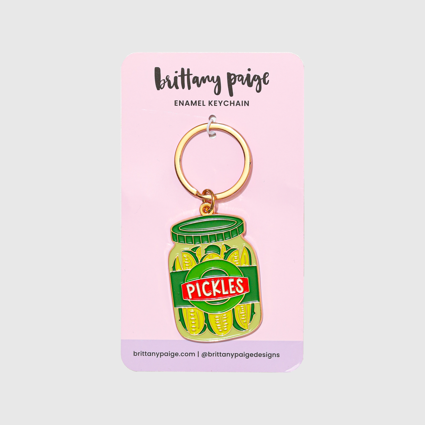 Enamel keychain of a pickle jar on a pink card with 'brittany paige' branding.