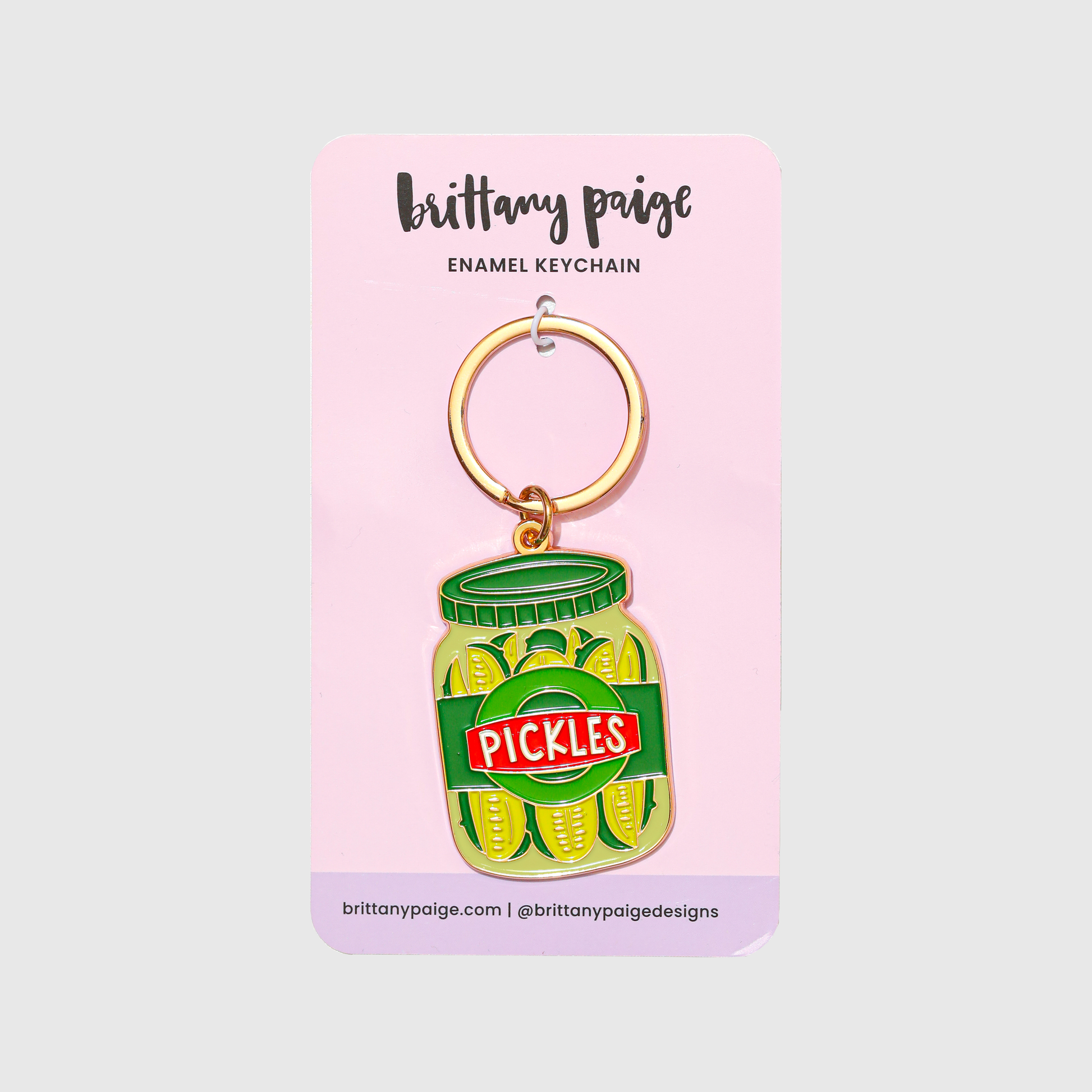 Enamel keychain of a pickle jar on a pink card with 'brittany paige' branding.
