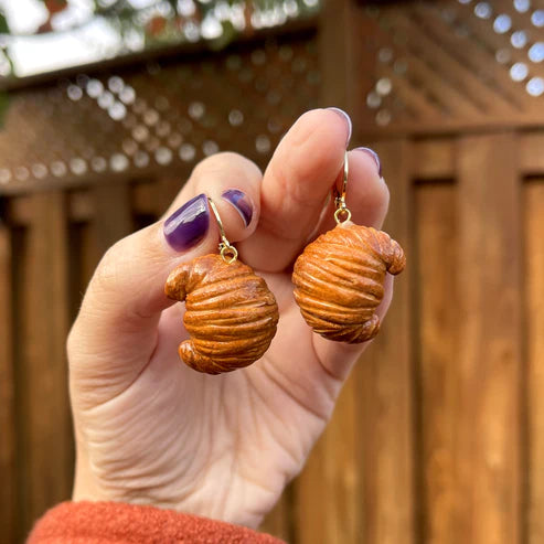 Hand holding earrings that look like a plain croissant 