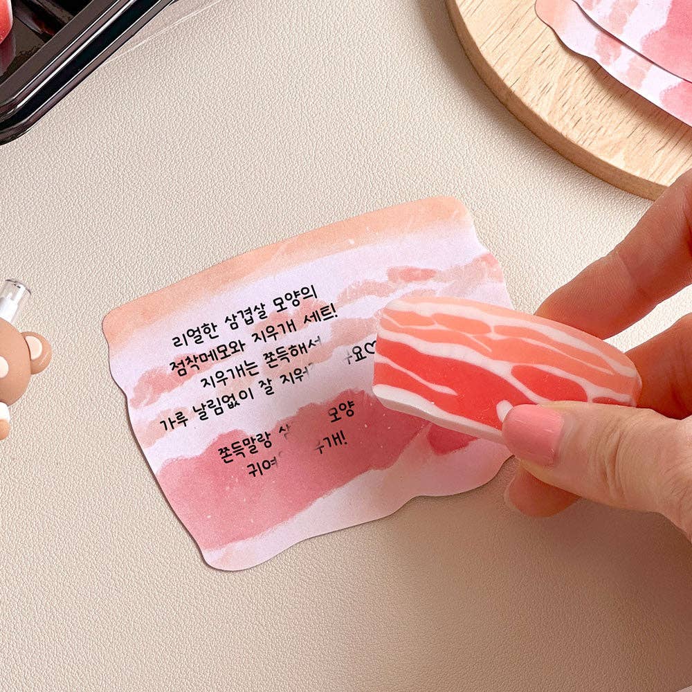 Hand holding an eraser that looks like pork belly over a memo note with text on a light surface.