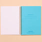 Open spiral-bound notebook with blue cover and white pages on a beige background