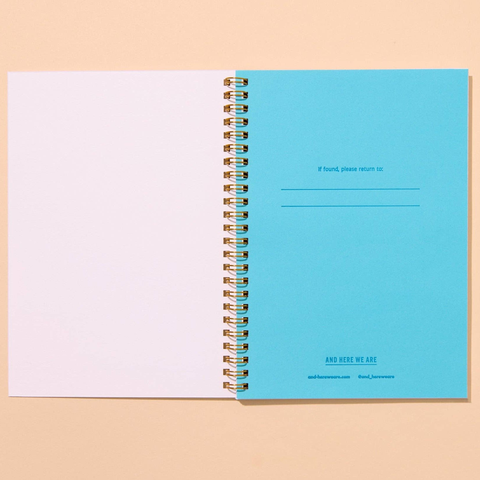 Open spiral-bound notebook with blue cover and white pages on a beige background