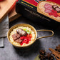 Candle shaped like a pot of ramen with ingredients on a dark surface, next to its packaging.