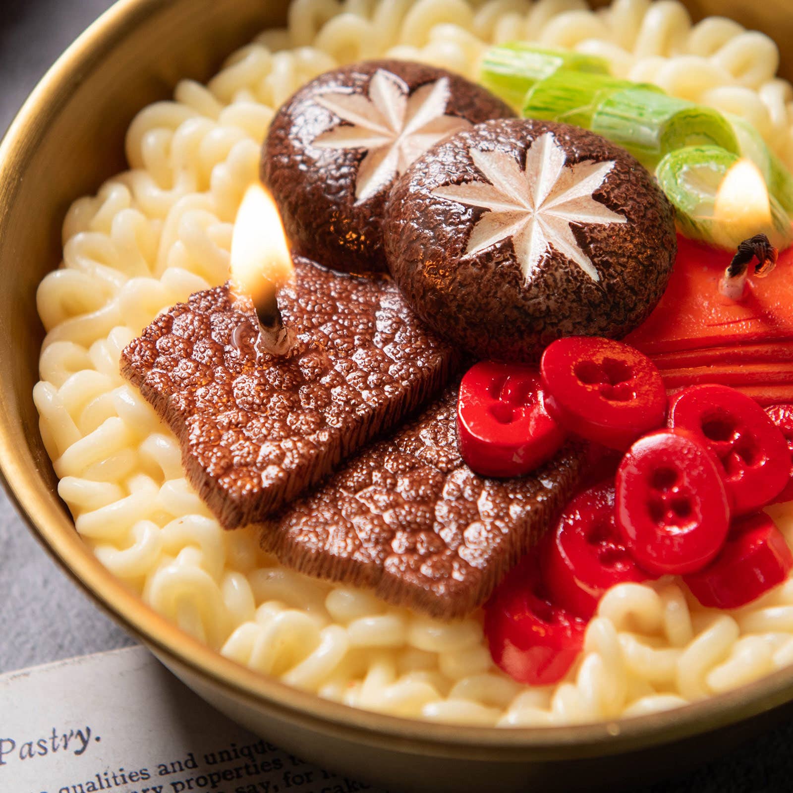 Close up of ramen noodles in gold pot with sliced beef, red peppers, and green onions