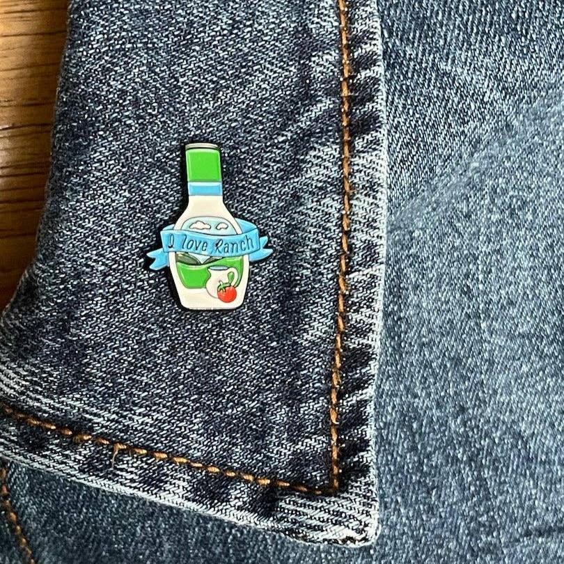 Ranch bottle lapel pin that has a ribbon across the bottle that says "I love Ranch" pinned on a jean jacket's lapel.