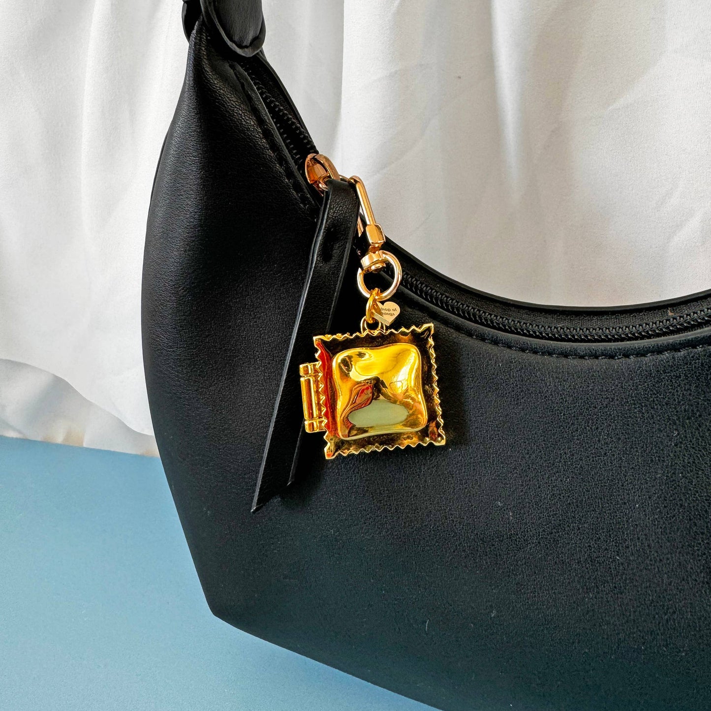 Black handbag with a gold ravioli locket charm on a white background