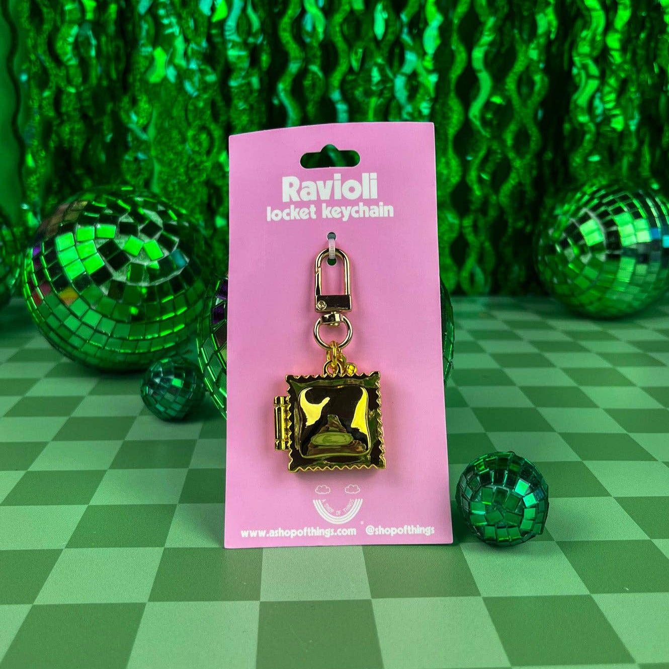 Gold ravioli locket keychain on a pink card with green disco balls in the background