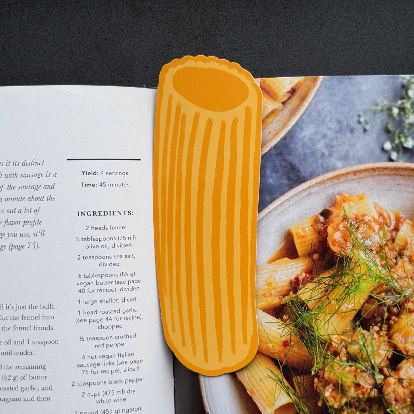Pasta-shaped bookmark on an open cookbook with pasta dish in the background