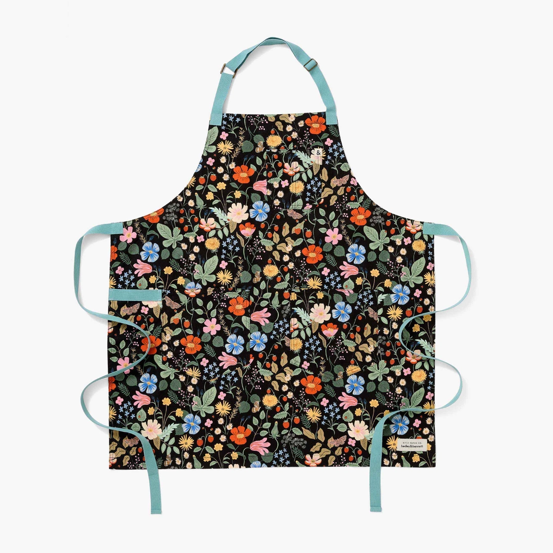 Flat image of apron with colorful design pattern of bright florals and foliage and light blue neck and waist straps 