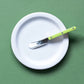 Sage colored background with a white plate on top. Lime green sabre spreader is resting on the plate.