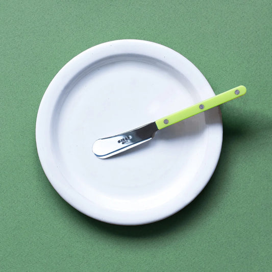 Sage colored background with a white plate on top. Lime green sabre spreader is resting on the plate.