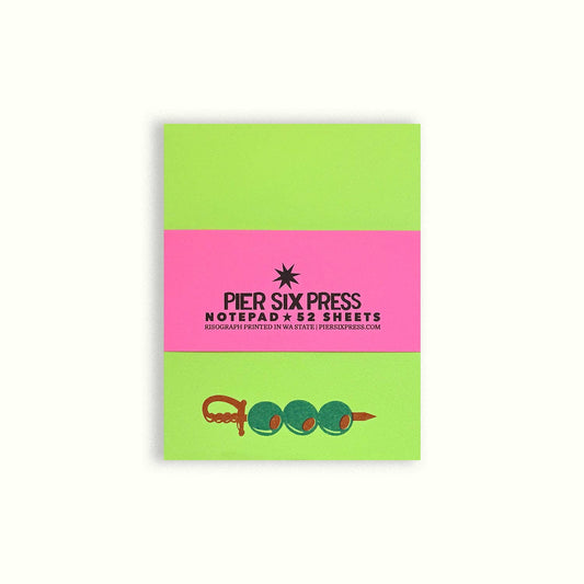 Pier Six Press notepad with green and pink design and a skewer of olives at the bottom on a white background
