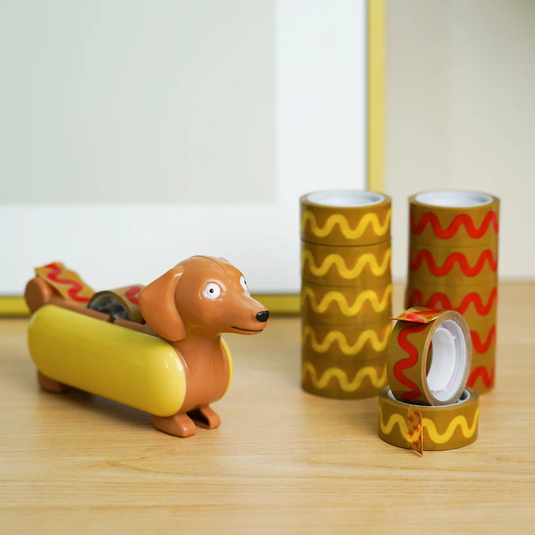 tape dispenser designed to look like a wiener dog in a hot dog bun and the tape designed to look like the ketchup (or mustard) on top