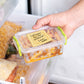Hand holding a food container with a 'Leftovers for the weekend! Love, Mom' ravioli sticky note inside a refrigerator.