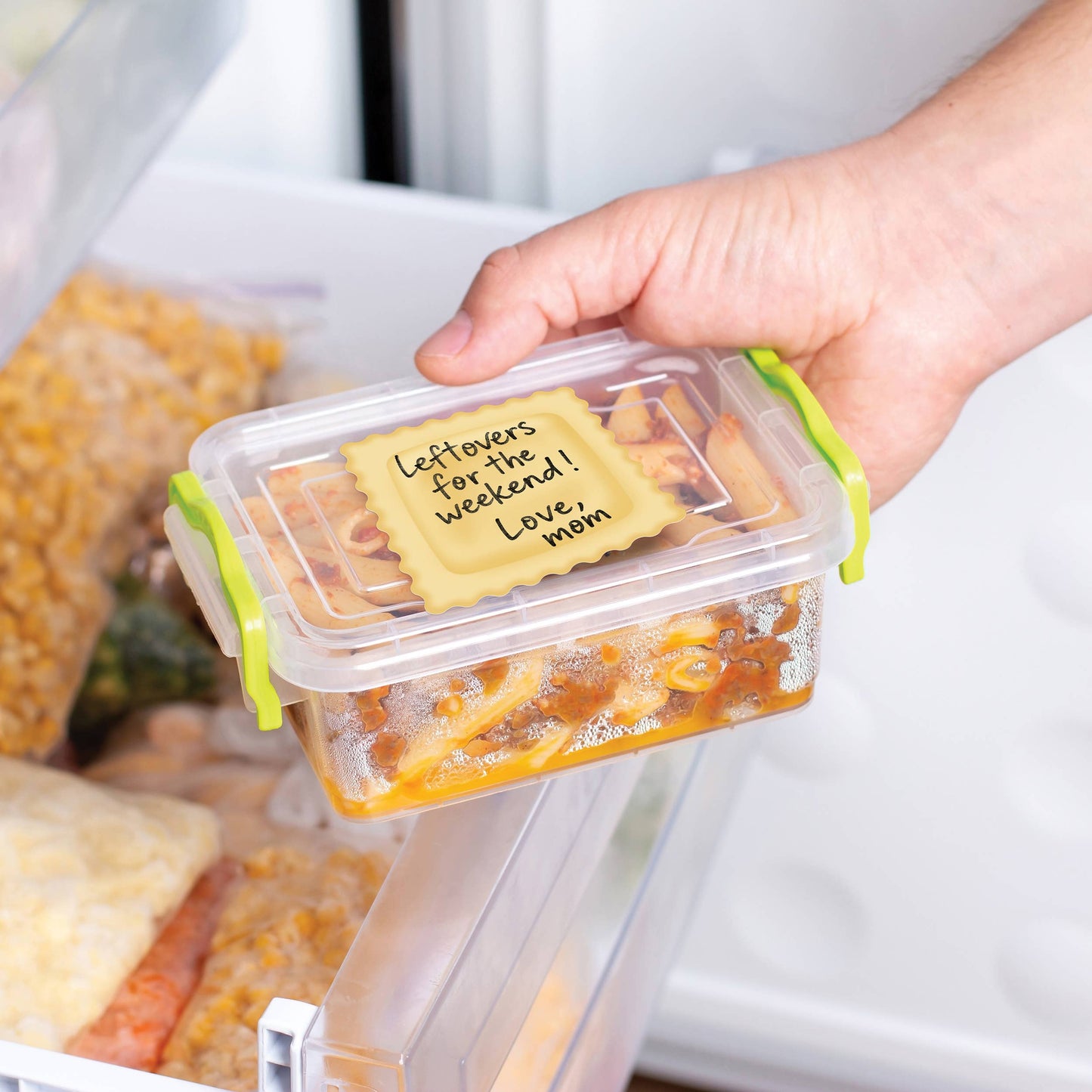 Hand holding a food container with a 'Leftovers for the weekend! Love, Mom' ravioli sticky note inside a refrigerator.
