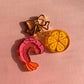 Three colorful charms, shrimp, lemon and bow on a pink background