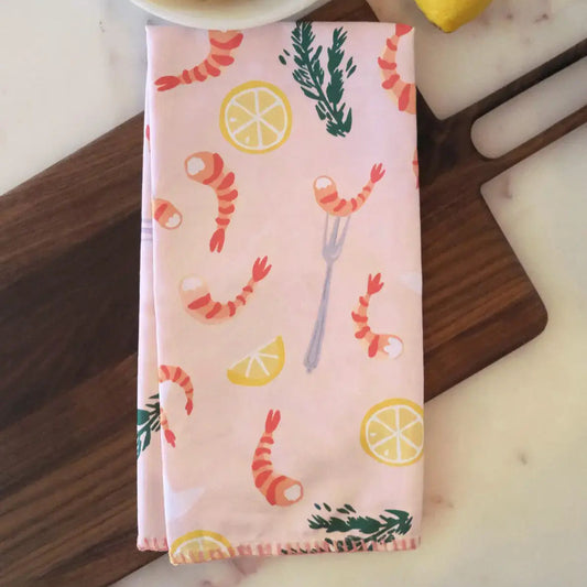 Kitchen tea towel, light pink/salmon in color with a design of illustrated lemon halves and wedges, shrimp, cocktail fork and herbs