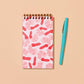spiral bound pocket notebook featuring a shrimp design next to a blue pen 