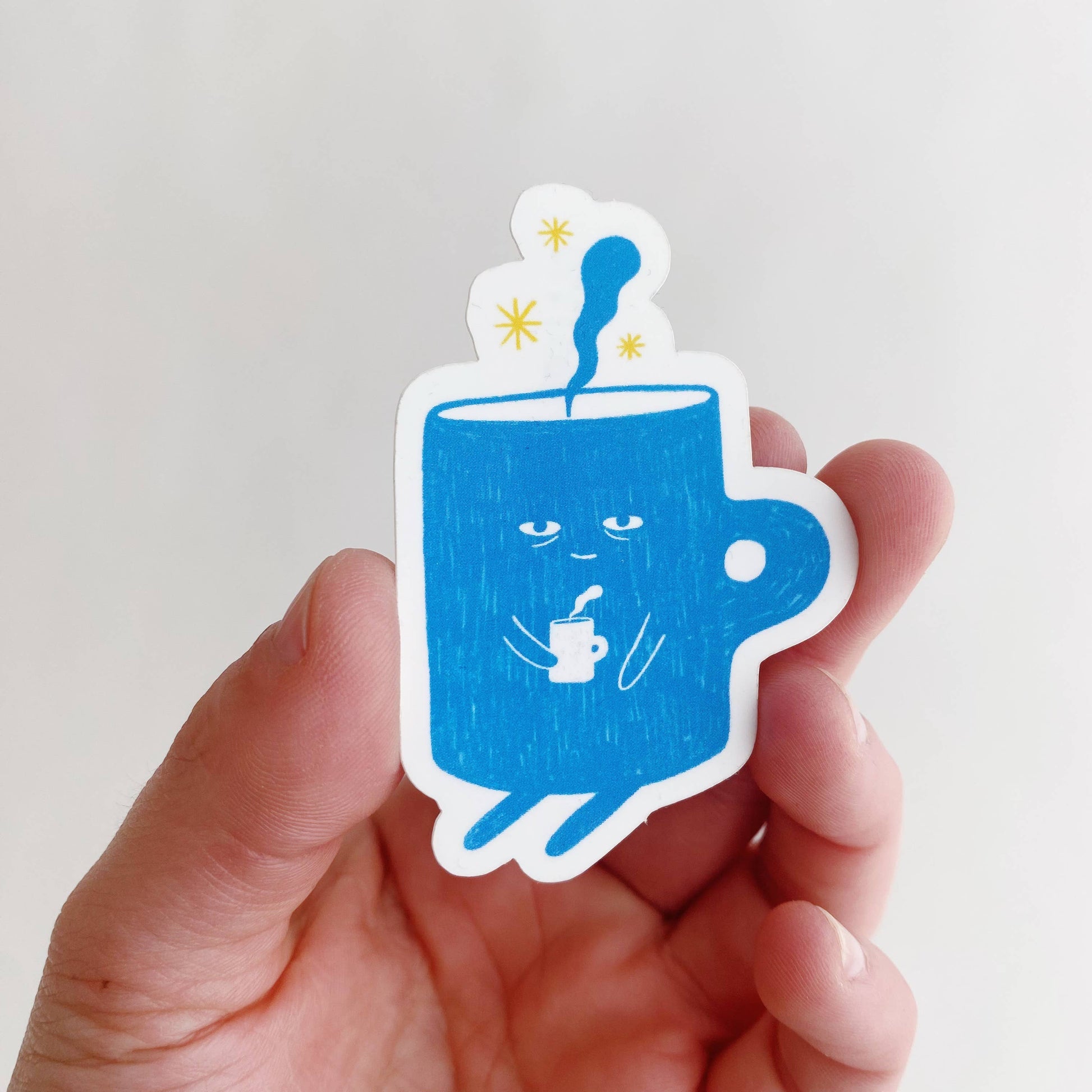 sticker with a blue, sleepy mug/cup of coffee on it who is also holding a hot cup of coffee