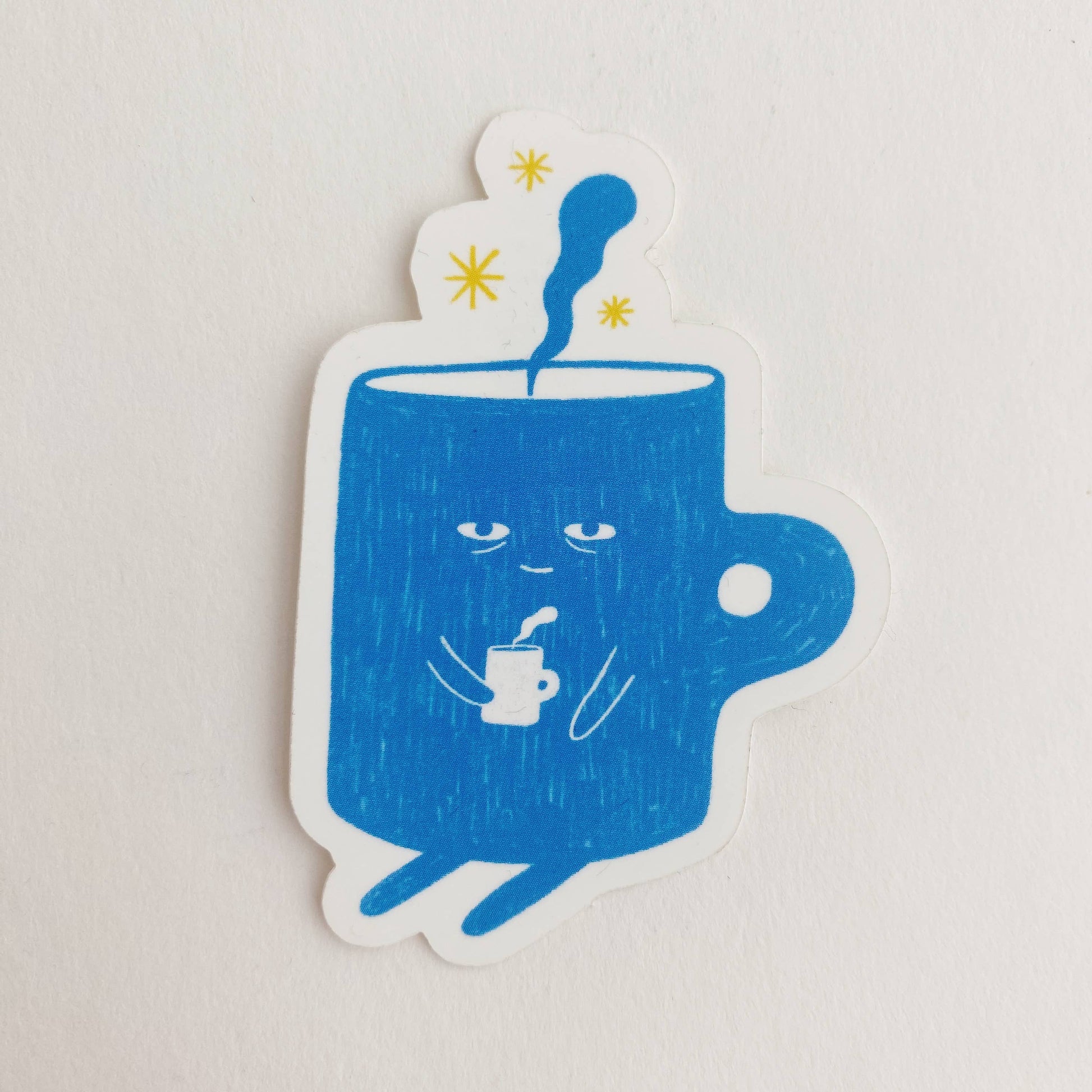 sticker with a blue, sleepy mug/cup of coffee on it who is also holding a hot cup of coffee