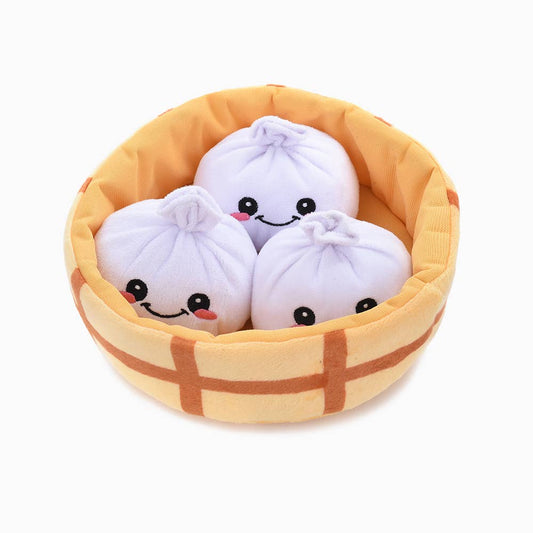 Plush soup dumplings in a steamer basket on a white background