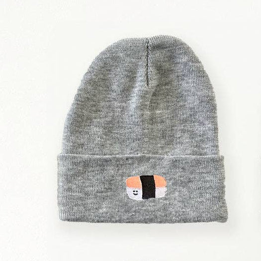 Four knit beanie hats arranged in a 2x2 grid on a white background, each with a small embroidered spam musubi-themed patch on the cuff. The top-left beanie is heather gray, the top-right is olive green, the bottom-left is black, and the bottom-right is off-white/cream.