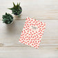 Greeting card with red chili pepper pattern and text "you spice up my life. Happy Valentine's!" on a wooden surface with small plants