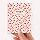 Card with red chili pepper pattern and text on a light pink background, held by a hand.