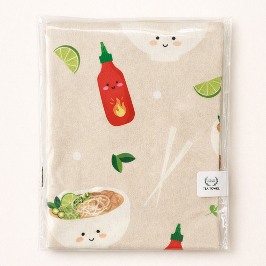 Beige tea towel with pho bowls and sriracha illustrations in packaging