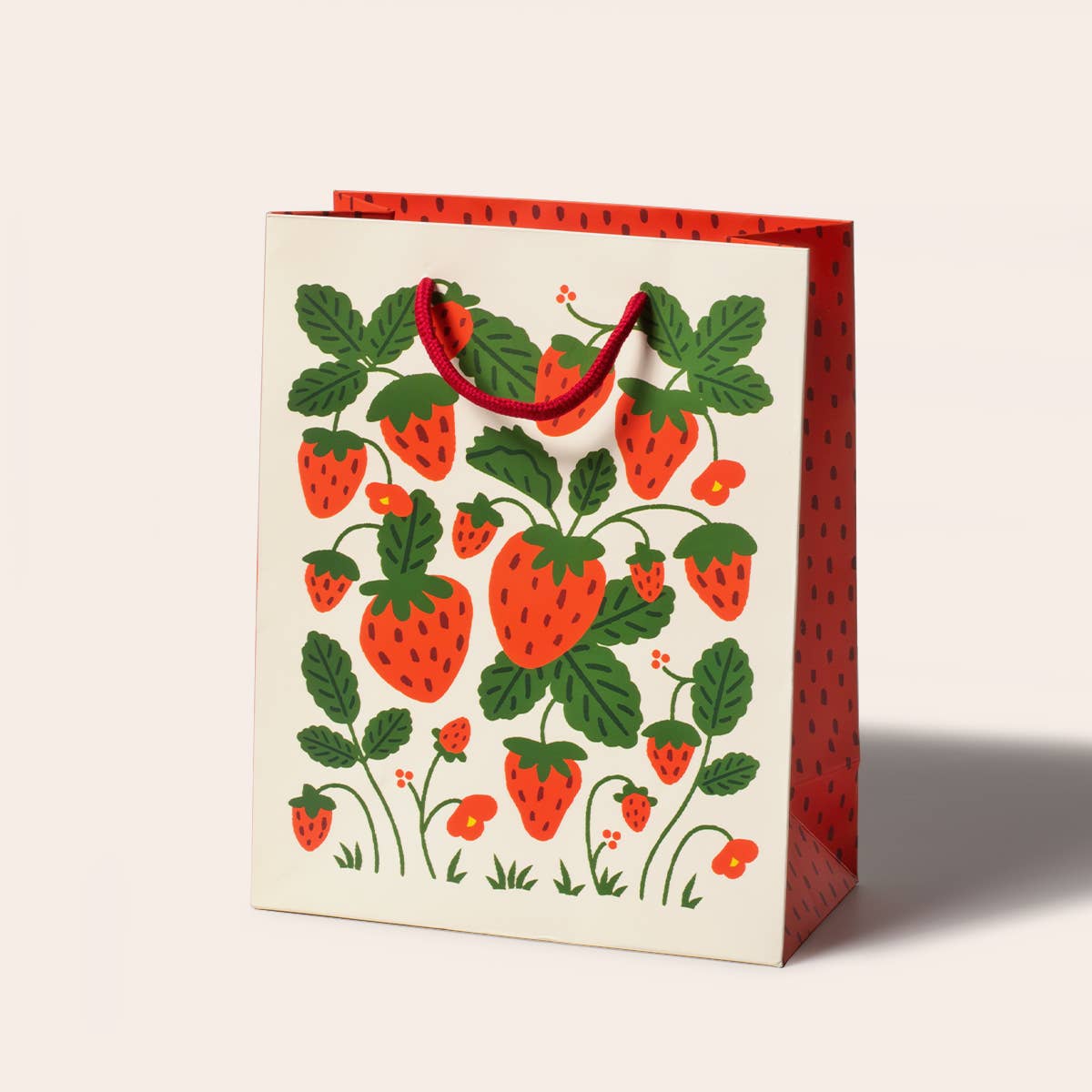 strawberries gift bag design is composed of a white background on the main side with strawberries with stems and leaves still. The sides and inside of the bag is red and covered with strawberry seeds