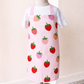 Pink apron with strawberry pattern on a mannequin against a white wall.