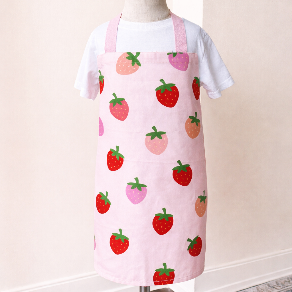 Pink apron with strawberry pattern on a mannequin against a white wall.