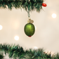 Green glittery stuffed olive Christmas ornament hanging on a tree branch with lights in the background