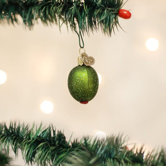 Green glittery stuffed olive Christmas ornament hanging on a tree branch with lights in the background