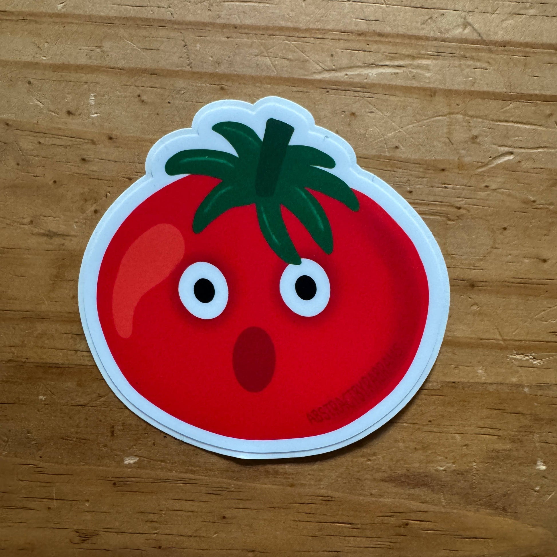 Cartoon tomato sticker with a surprised expression on a wooden surface