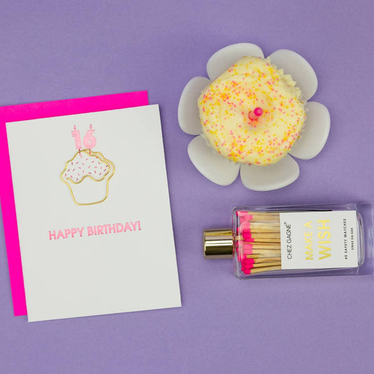 Happy Birthday card, cupcake-shaped paper clip/illustration, and matchbox with matches on a purple background