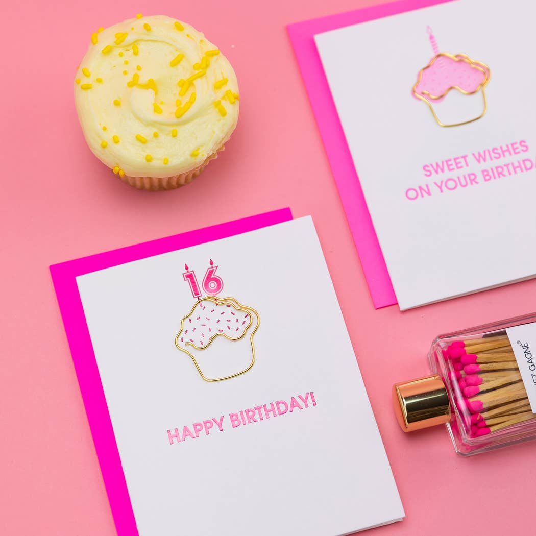 Two birthday cards with cupcake illustrations, a cupcake, and matches on a pink background.